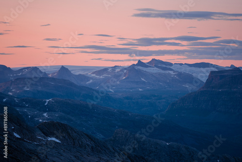 Midnight sun in arctic summer landscape of Norway. Silhouettes of mountain ranges in sunset colours of blue, orange and purple. Few clouds on clear dawn and dusk sky. Moody mountain range landscape photo