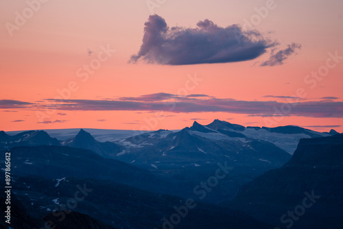 Midnight sun in arctic summer landscape of Norway. Silhouettes of mountain ranges in sunset colours of blue, orange and purple. Few clouds on clear dawn and dusk sky. Moody mountain range landscape photo