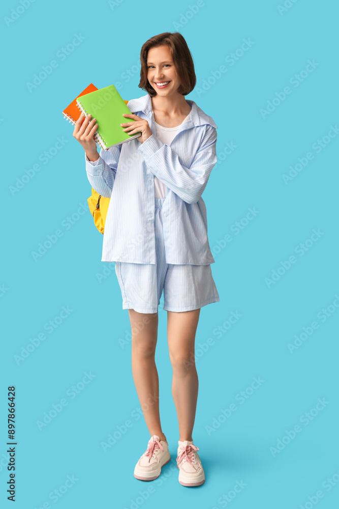 Beautiful female student with backpack and notebooks on blue background Beautiful female student with backpack and notebooks on blue background