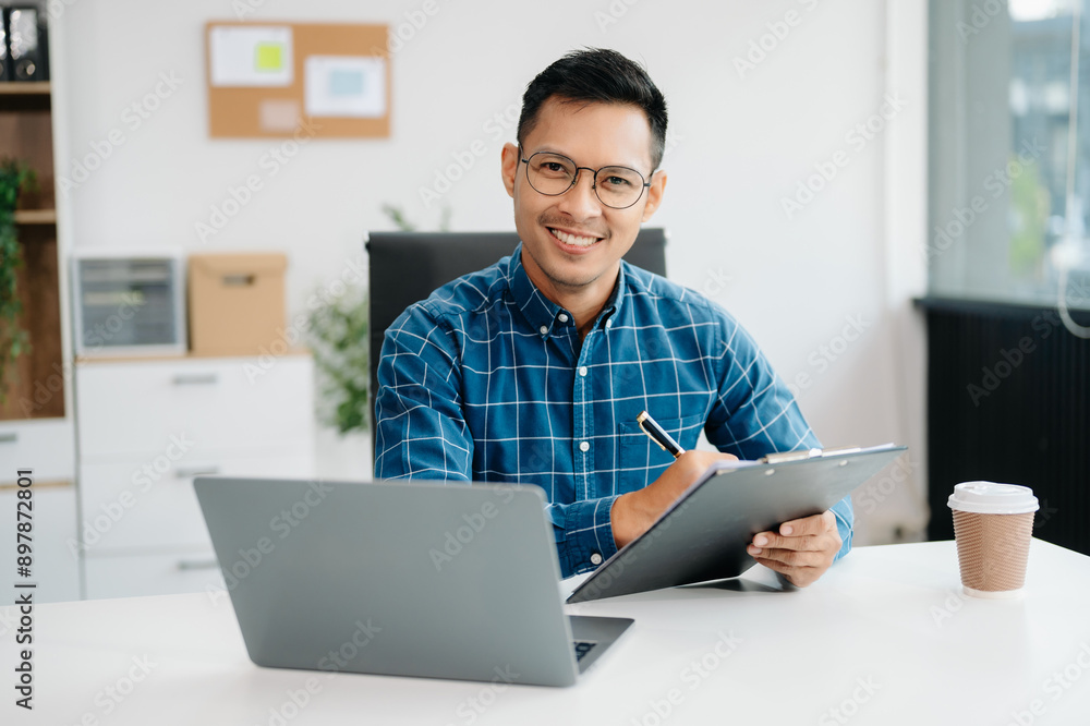 Young handsome man typing on tablet and laptop while sitting at the working table office Young handsome man typing on tablet and laptop while sitting at the working table office