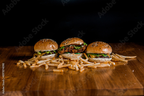 three hamburgers and a side of french fries on a wooden table photo