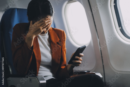 Obraz na płótnie Stressed and serious young asian businesswoman remote working on the plane, suffering from headache and airsick during the flight