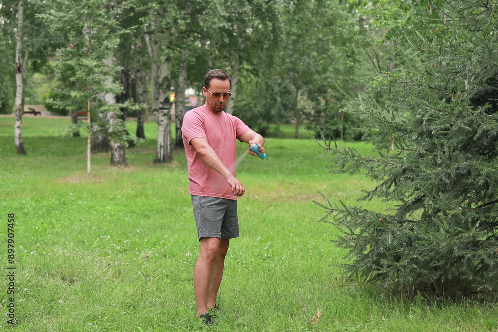a man sprays protective repellent on his skin and clothes while walking in the park a man sprays protective repellent on his skin and clothes while walking in the park