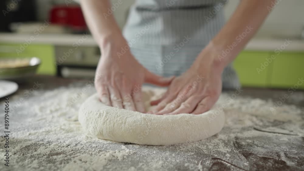 A female chef is kneading dough with her hands in the kitchen for making homemade pizza. A female chef is kneading dough with her hands in the kitchen for making homemade pizza.