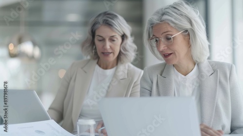 Two professional employees discussing a finance project on a laptop, soft-focus corporate boardroom.