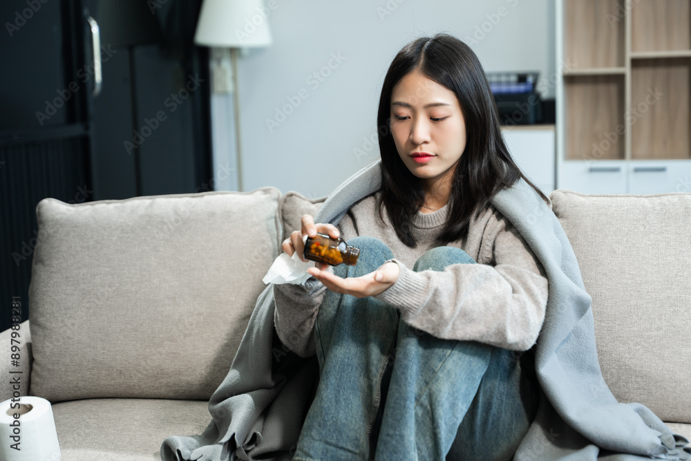 Young Asian woman suffering from flu symptoms, covered with a blanket on a sofa. Concept of illness, healthcare, and recovery Young Asian woman suffering from flu symptoms, covered with a blanket on a sofa. Concept of illness, healthcare, and recovery