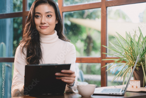 Asian woman working online by laptop and notebook at cafe. Young businesswoman are happy and smile using technology for communication  finance  student and reading.