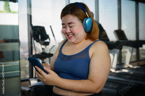 Asian woman relax after workout in gym. Asian woman using mobile phone and listen music at gym.