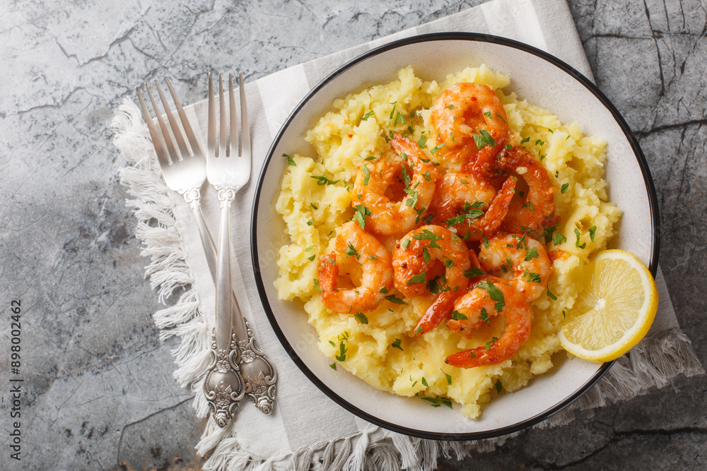 Portion of garlic shrimps with mashed potatoes, lemon and herbs close-up in a bowl on the table. Horizontal top view from above Portion of garlic shrimps with mashed potatoes, lemon and herbs close-up in a bowl on the table. Horizontal top view from above