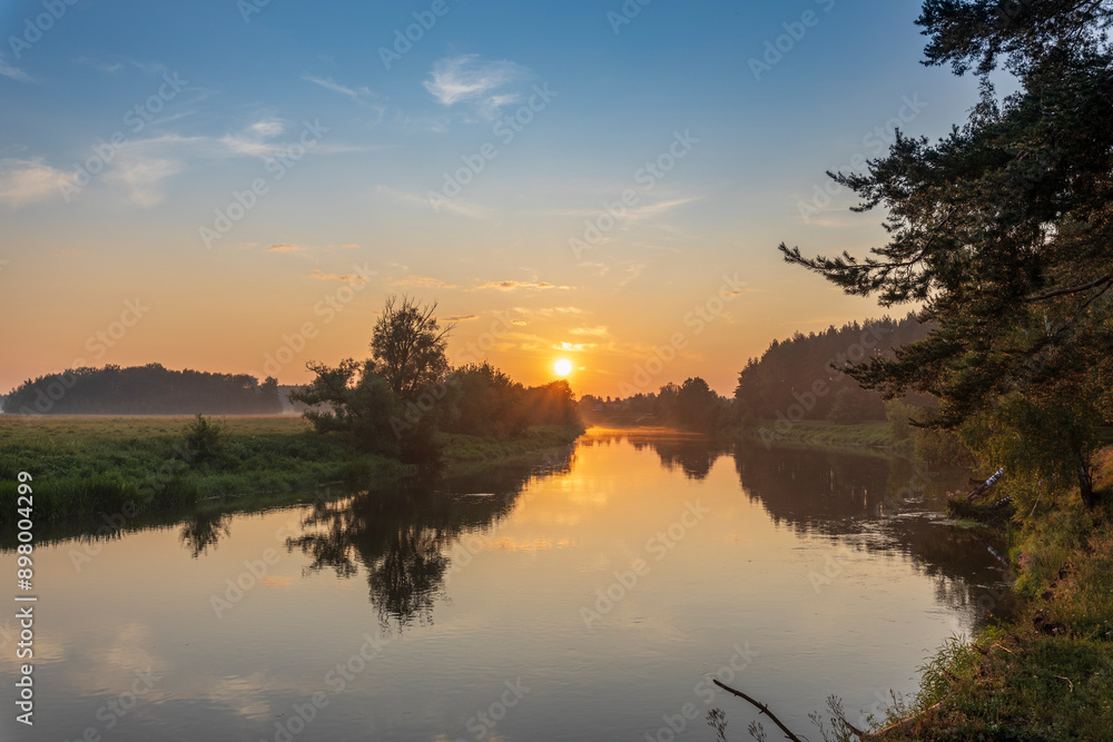 A beautiful sunset over a river with trees in the background A beautiful sunset over a river with trees in the background