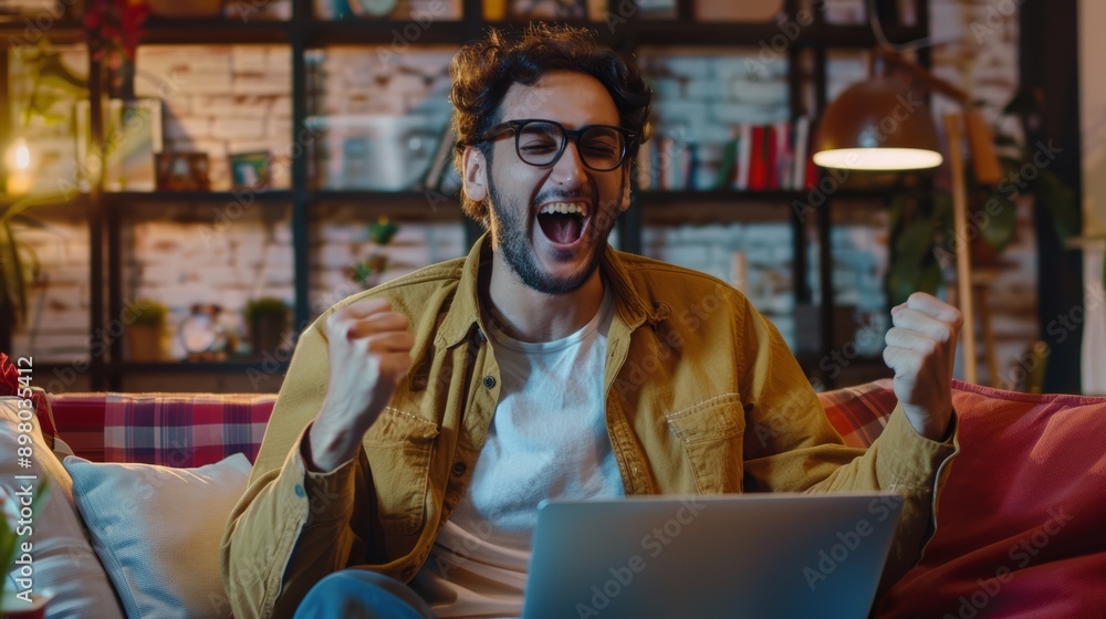 Portrait of happy man sitting at home on the sofa, working with laptop and celebrating success, victory, rejoicing.