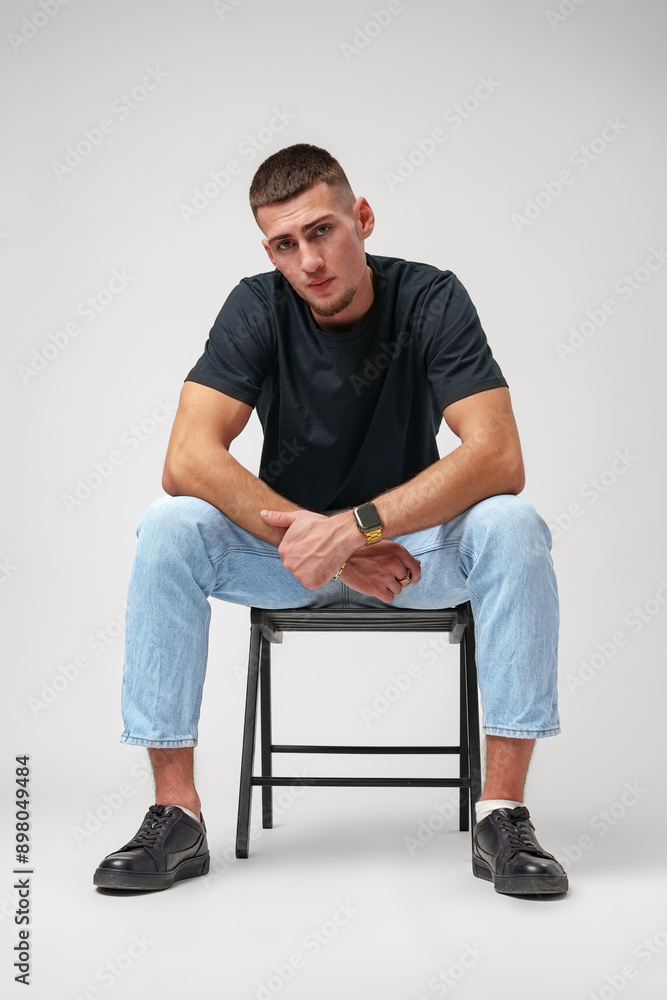 Young Man Sitting on a Stool Against a White Background Young Man Sitting on a Stool Against a White Background