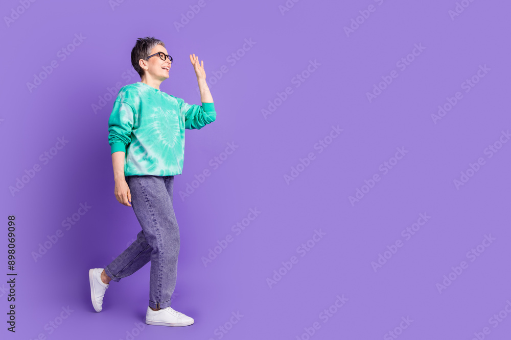 Full body photo of attractive senior woman walking wave hand dressed stylish green clothes isolated on purple color background Full body photo of attractive senior woman walking wave hand dressed stylish green clothes isolated on purple color background