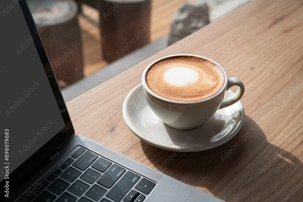 Close-up of Hot coffee latte with latte art milk foam in cup mug and laptop computer on wood desk office desk in coffee shop at the cafe,during business work concept