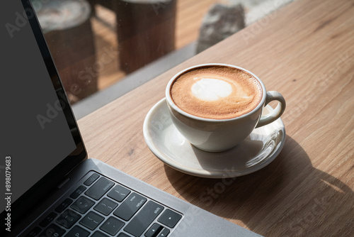 Obraz na płótnie Close-up of Hot coffee latte with latte art milk foam in cup mug and laptop computer on wood desk office desk in coffee shop at the cafe,during business work concept w salonie