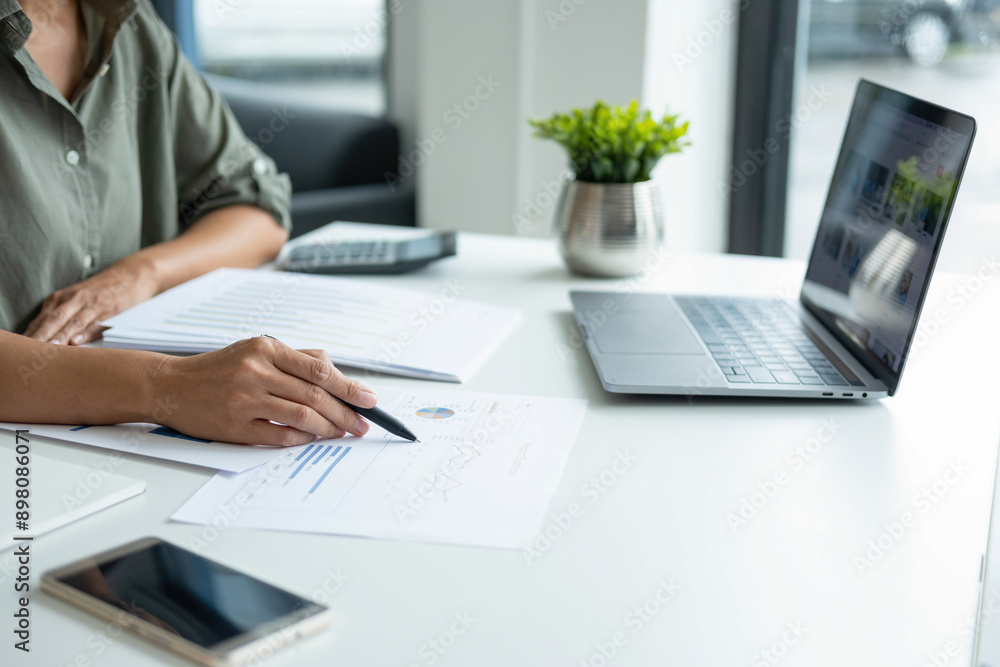 Businesswoman sitting at desk on couch in workplace or at home working on laptop and analyzing data on charts and graphs and writing on papers to make business plan and strategies for company, Businesswoman sitting at desk on couch in workplace or at home working on laptop and analyzing data on charts and graphs and writing on papers to make business plan and strategies for company,