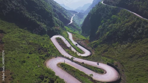 This footage captures the breathtaking winding road through the lush green mountains of Ha Giang, North Vietnam. The shot highlights the dramatic curves of the road as vehicles navigate it.