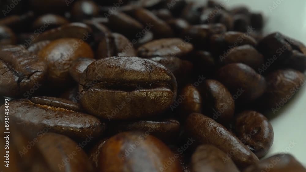 Macro of coffee bean scattering at spoon with zoom out camera. Close up of white spoon scooping brown coffee seeds scattering with blurring black background. Caffeine energy drink concept. Pabulum. Macro of coffee bean scattering at spoon with zoom out camera. Close up of white spoon scooping brown coffee seeds scattering with blurring black background. Caffeine energy drink concept. Pabulum.