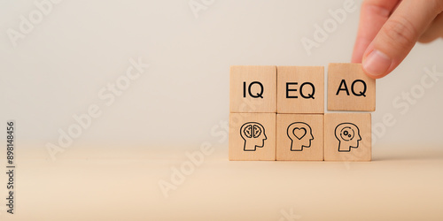 Wooden blocks with the letters IQ, EQ and AQ representing Intelligence Quotient, Emotional Quotient, Adaptability Quotient. A hand adjusting AQ block, symbolizing adaptability in modern intelligence.