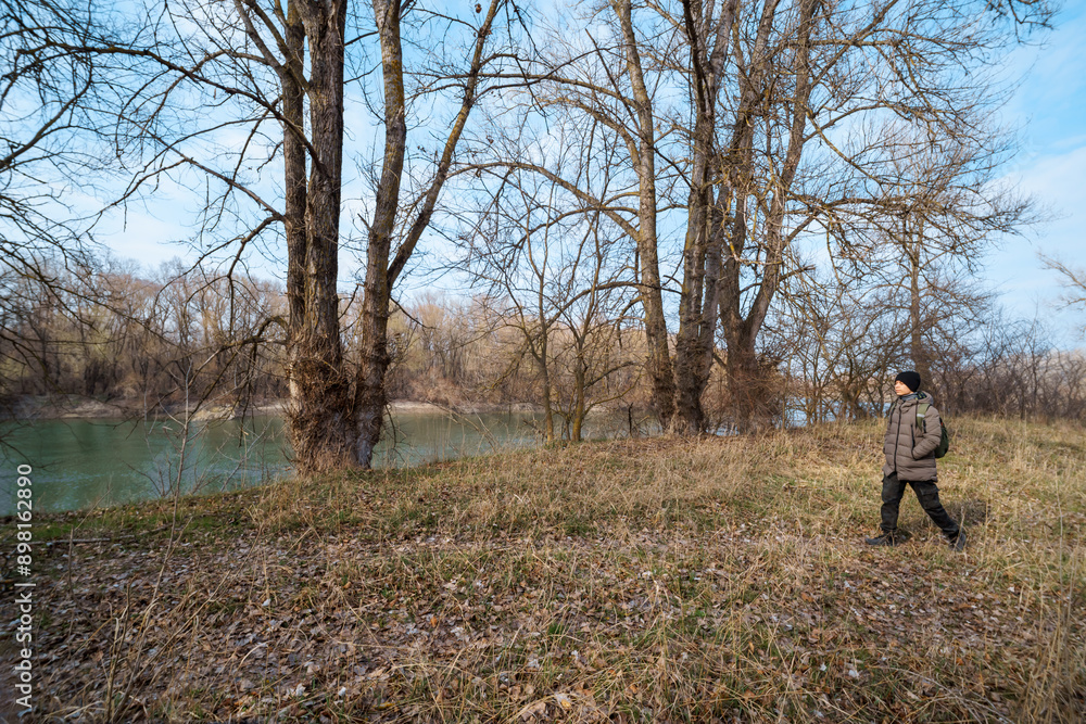 A teenage boy walking along the riverbank and forest, early spring landscape, the concept of hiking and outdoor activities A teenage boy walking along the riverbank and forest, early spring landscape, the concept of hiking and outdoor activities