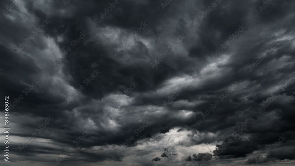 Fototapeta premium dark dramatic sky with black stormy clouds before rain or snow as abstract background, extreme weather, the sun shines through the clouds, high contrast photo