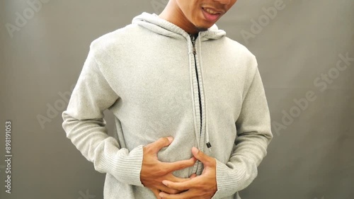 The young man wearing a gray sweater grimaced while holding his aching stomach
