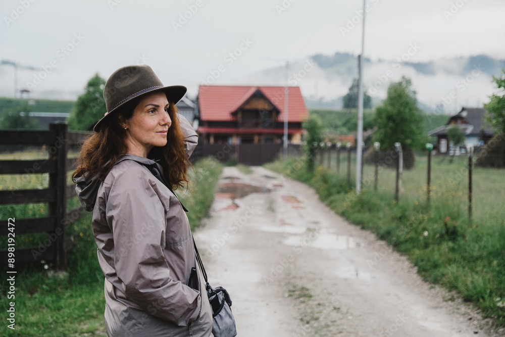 Fototapeta premium Young woman standing near house in mountain village in summer. Summer trip on mountain routes in Europe.