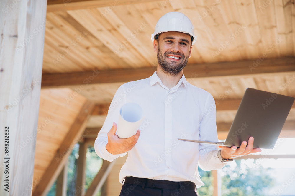 Man builder. Foreman with laptop. Contractor for construction company. Architect in unfinished building. Builder in wooden modular house under construction. Man engineer from construction team Man builder. Foreman with laptop. Contractor for construction company. Architect in unfinished building. Builder in wooden modular house under construction. Man engineer from construction team