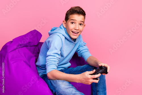 Photo portrait of cute teen boy beanbag hold joystick play videogame dressed stylish blue clothes isolated on pink color background photo