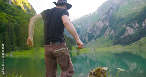 A man jumps on an old stump by the lake with outstretched arms and enjoys nature.