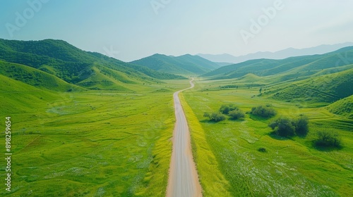  A bird's-eye perspective of a dirt path in a lush green valley, surrounded by distant mountains and nearer verdant grass