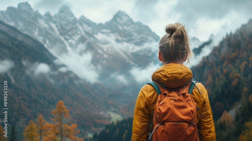 A woman with a backpack stands before towering mountain ranges A woman with a backpack stands before towering mountain ranges