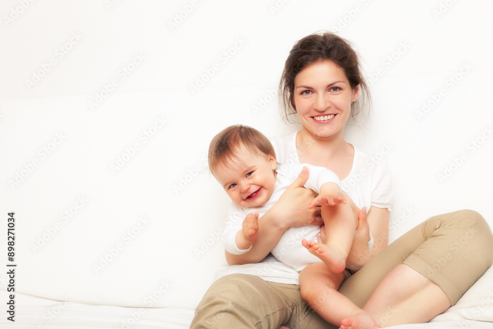 Happy mother playing with baby on white sofa Happy mother playing with baby on white sofa