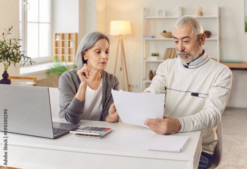 Elderly couple sits and working together at a table in home, reviewing bills, documents, payments, and managing their finances. They are engaged in a shared effort to handle financial matters. Elderly couple sits and working together at a table in home, reviewing bills, documents, payments, and managing their finances. They are engaged in a shared effort to handle financial matters.