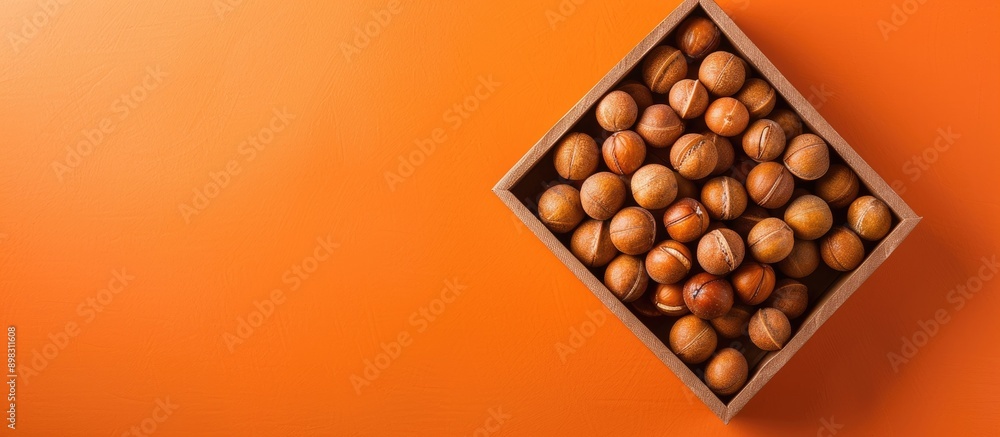 A box of natural macadamia nuts on an orange background captured from above with ample copy space image A box of natural macadamia nuts on an orange background captured from above with ample copy space image