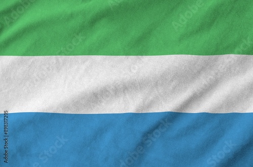 Sierra Leone flag depicted on folded wavy fabric of old cloth close up photo