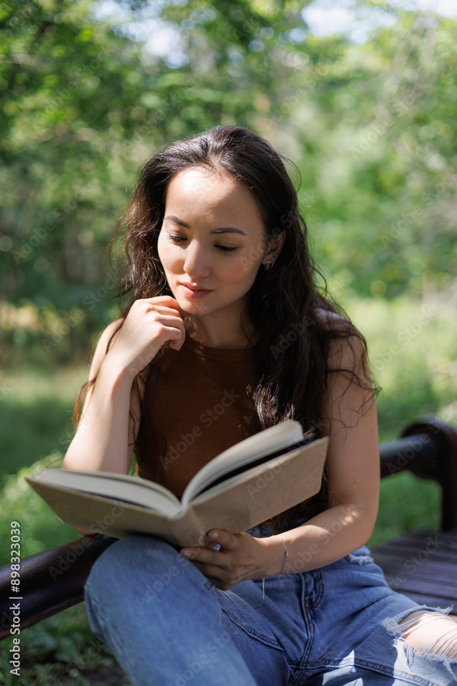 Obraz premium Portrait of asian woman reading blurred book on bench in park
