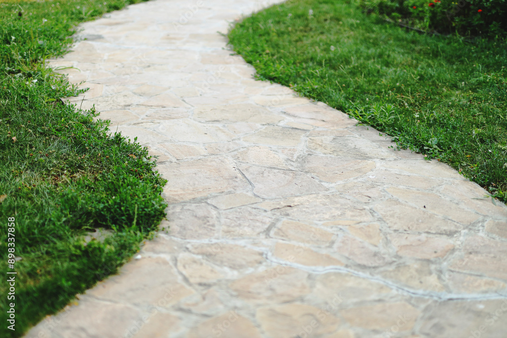 A stone walkway with grass on either side. The walkway is narrow and has a slight curve A stone walkway with grass on either side. The walkway is narrow and has a slight curve