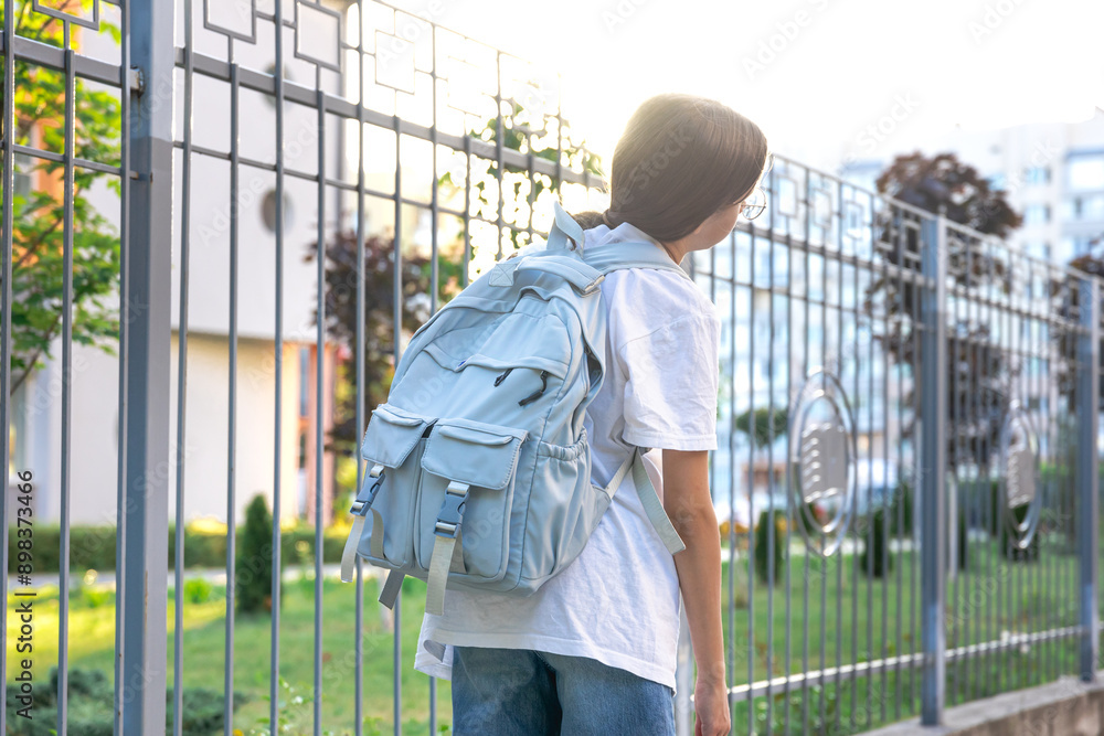Schoolgirl with a backpack on her shoulders. School on the background of the sunset. Back to school. Schoolgirl with a backpack on her shoulders. School on the background of the sunset. Back to school.