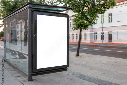 Blank White Bus Stop Vertical Poster Billboard Mockup On An Empty City Street. Advertising Lightbox On The Sidewalk With Car Light Trails In The Background