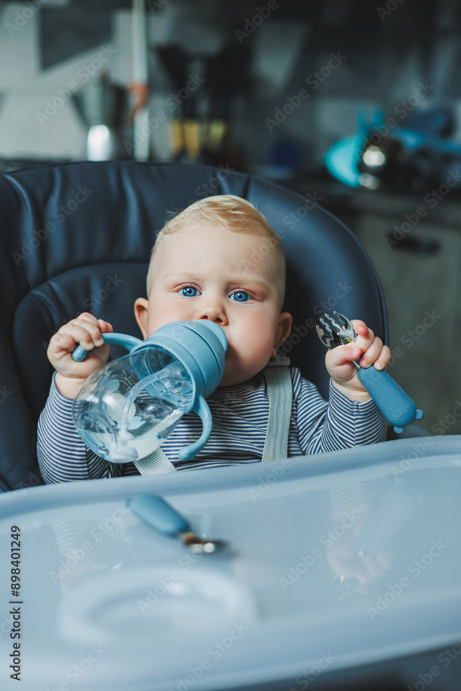 The baby drinks water from a plastic drinking cup with a straw. Tableware for babies. The baby drinks water from a plastic drinking cup with a straw. Tableware for babies.