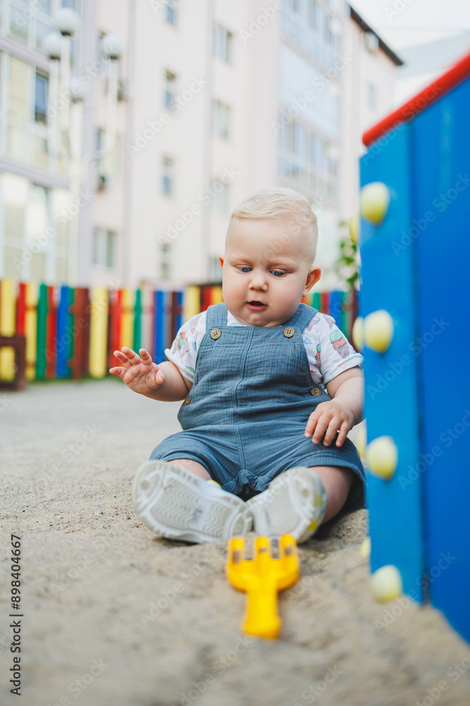 Fototapeta premium A 1-year-old child plays in the sandbox. A boy in summer clothes is playing on the street.
