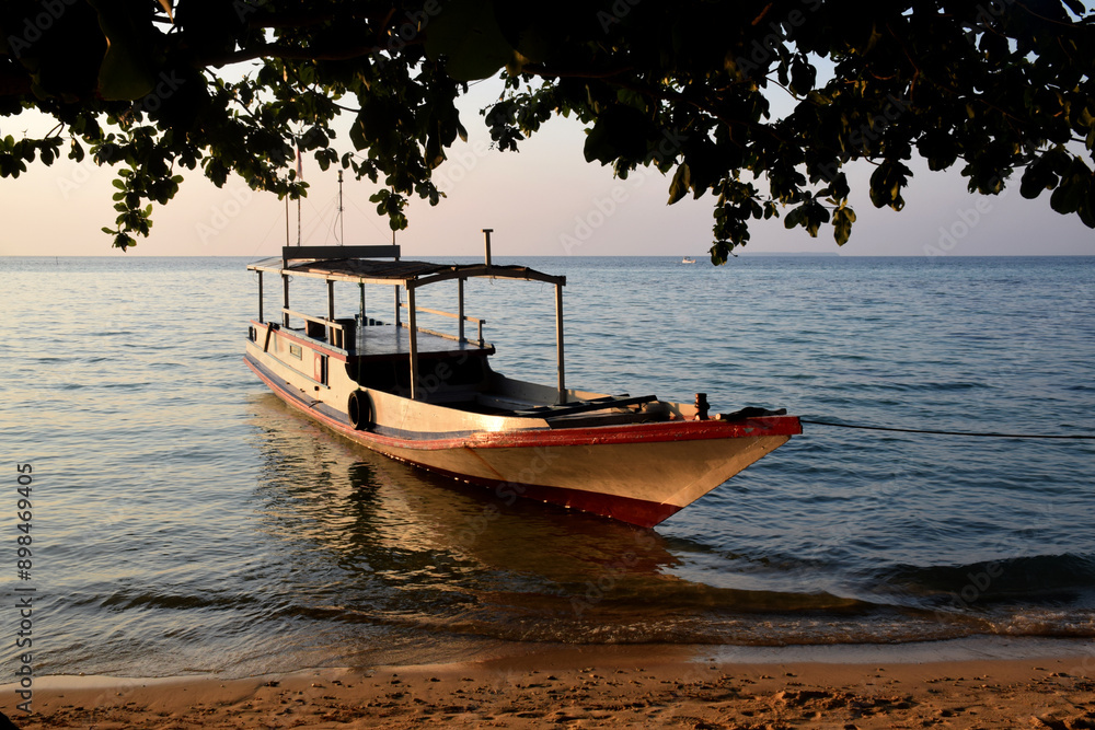 Fototapeta premium Boats on the edge of a clean beach, the rays of the setting sun