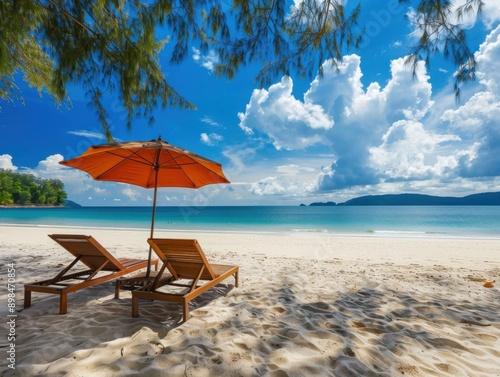 Idyllic tropical beach scene with two lounge chairs under an orange umbrella  overlooking the ocean with clear blue skies and fluffy clouds.