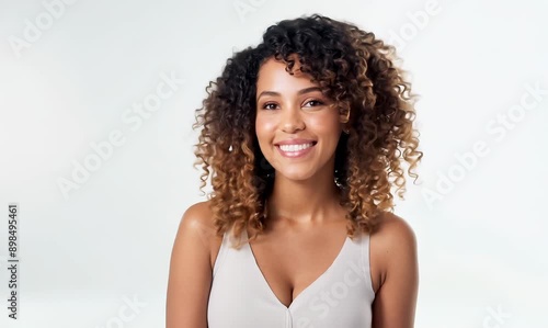Cheerful young adult woman with curly hair and smiling face standing in studio against white background