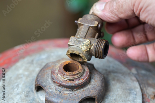 A broken valve of a gas cylinder in a hand against the background of a red gas cylinder. Propane gas leak and explosion concept. Copy space for text, industry. Safety precautions