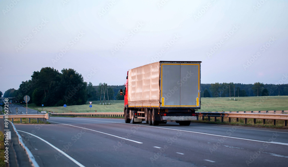 rear view of a truck with a semi-trailer walking along the road in the evening against the backdrop of nature and the sky. Cargo export and import concept. Copy space for text rear view of a truck with a semi-trailer walking along the road in the evening against the backdrop of nature and the sky. Cargo export and import concept. Copy space for text