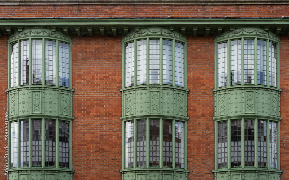Fototapeta premium Red brick building with 3 green windows showcasing a symmetrical facade