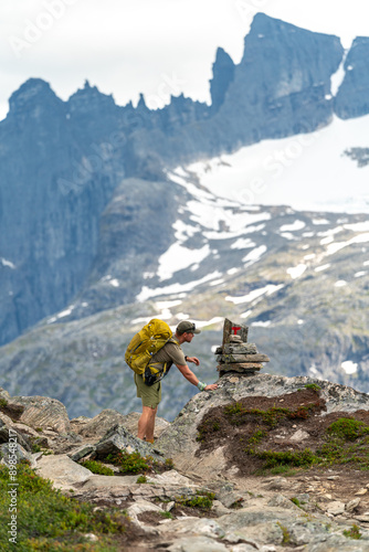 male backpacking hiker with yellow backpack climbing Romsdalseggen trail in Andalsnes Norway in summer with rocky mountains in the background photo