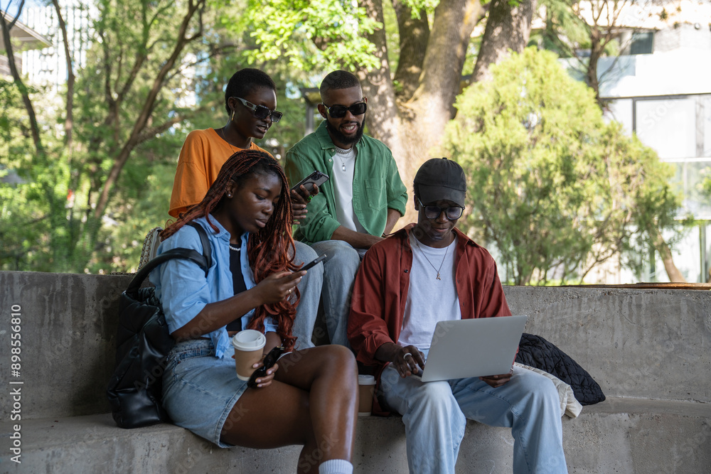 Relaxed company of african students chatting, resting, sitting outside on campus concrete staircase using smartphones. Calm quiet group of friends spending free time together before university classes Relaxed company of african students chatting, resting, sitting outside on campus concrete staircase using smartphones. Calm quiet group of friends spending free time together before university classes